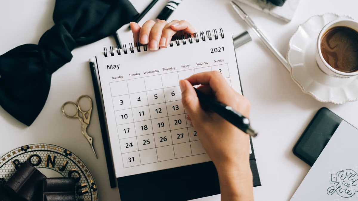 Top view of hands using a planner with coffee and accessories, focused on May 2021 calendar.